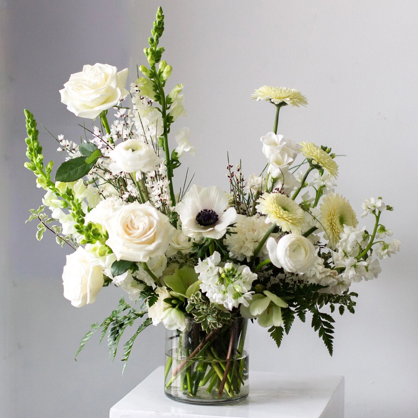 Modern white floral arrangement in glass vase by Annam Studio Toronto on white pedestal