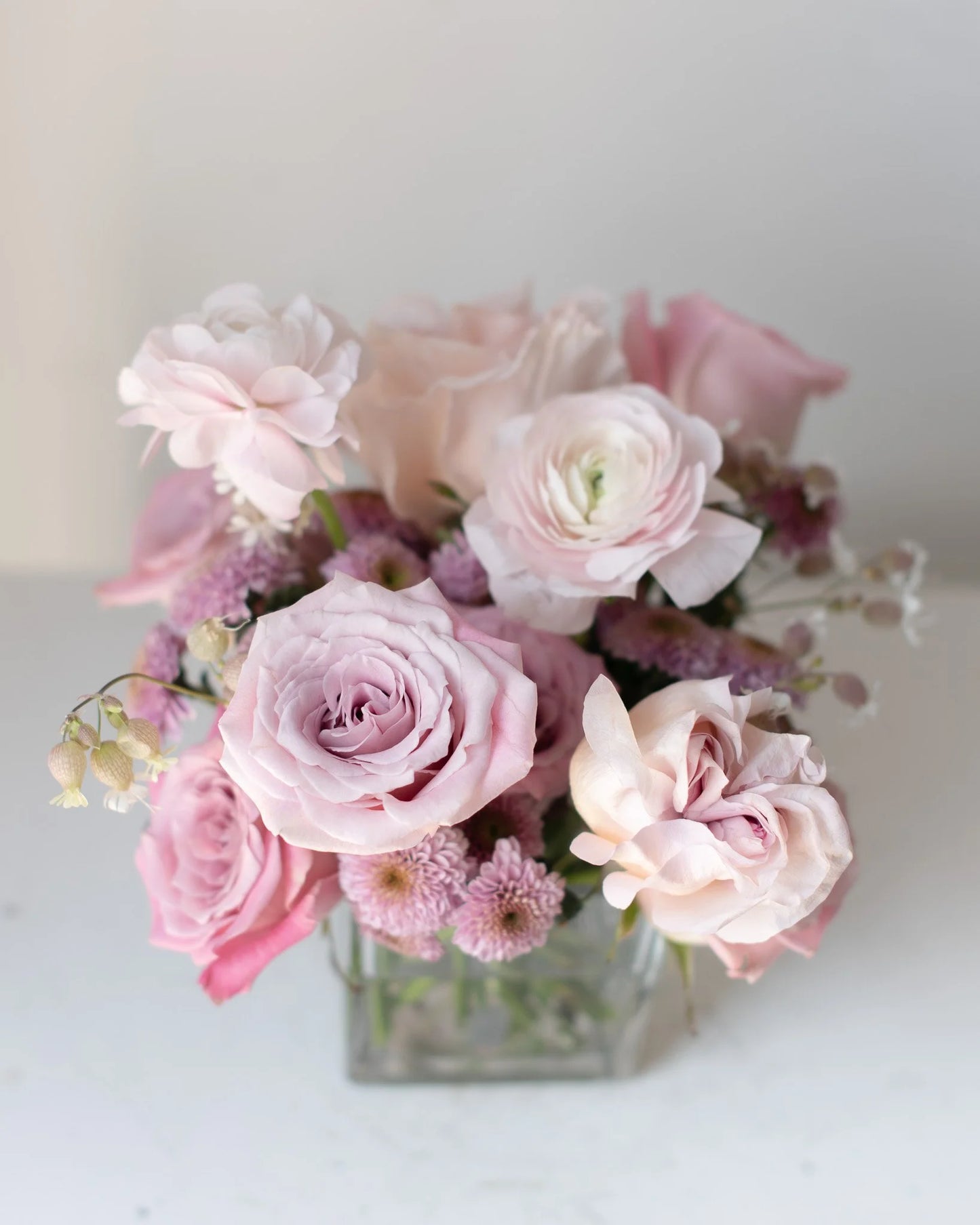Modern pink rose and ranunculus floral arrangement in square glass vase by Annam Studio