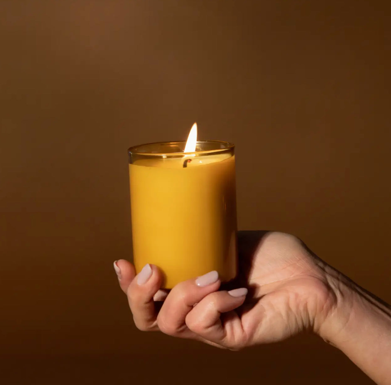 Hand holding a lit yellow glass candle, modern gift from Annam Studio Toronto
