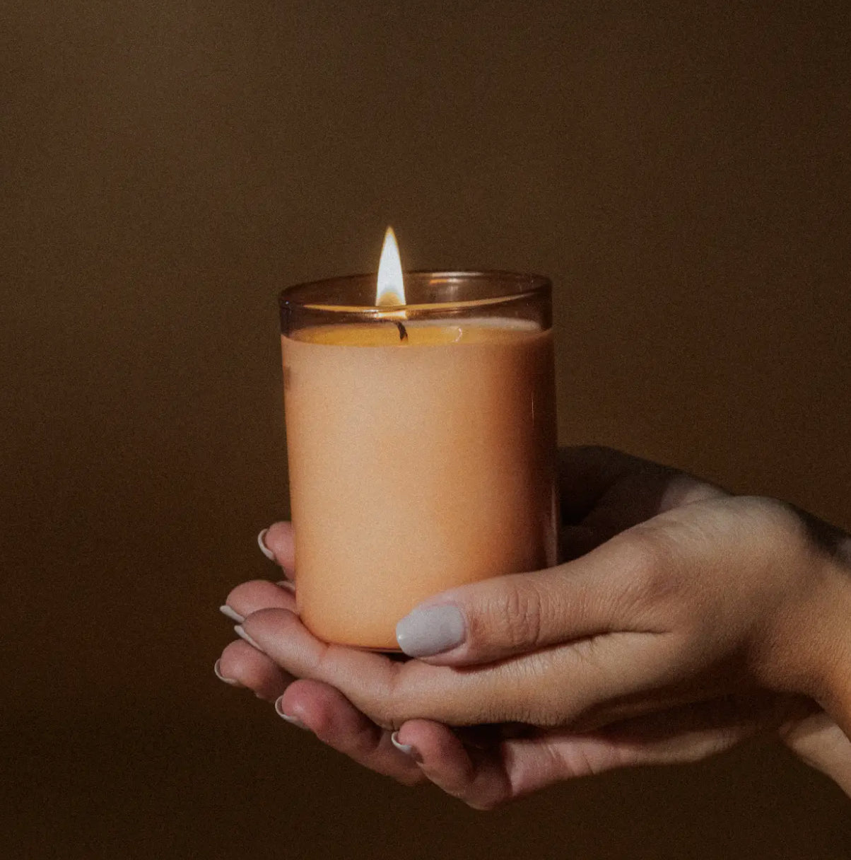 Hand holding a lit peach-colored candle, modern gift from Annam Studio Toronto.