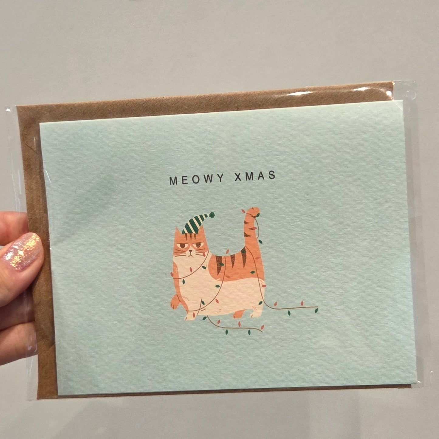 Holiday card with a cat illustration and 'MEOWY XMAS' text on a light blue background with an envelope for delivery or pickup in Toronto.