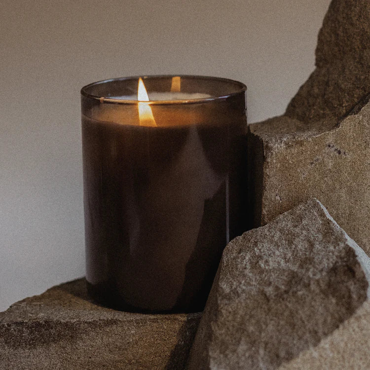 Scented brown glass candle burning on stone, modern floral decor from Annam Studio Toronto
