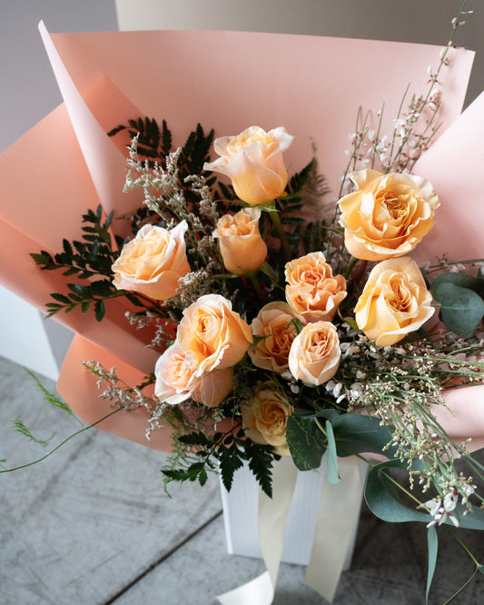 Bouquet of peach-colored roses with greenery in a pink paper wrap for delivery or pickup in Toronto.
