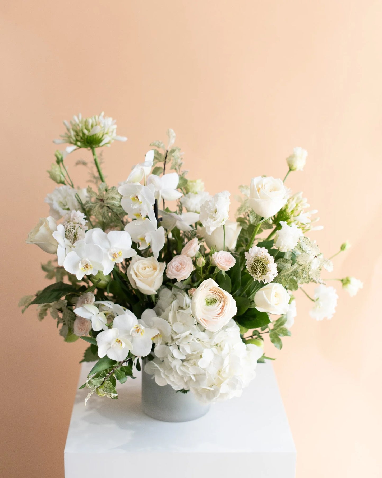 Modern white floral arrangement in a vase from Annam Studio, set against a peach background