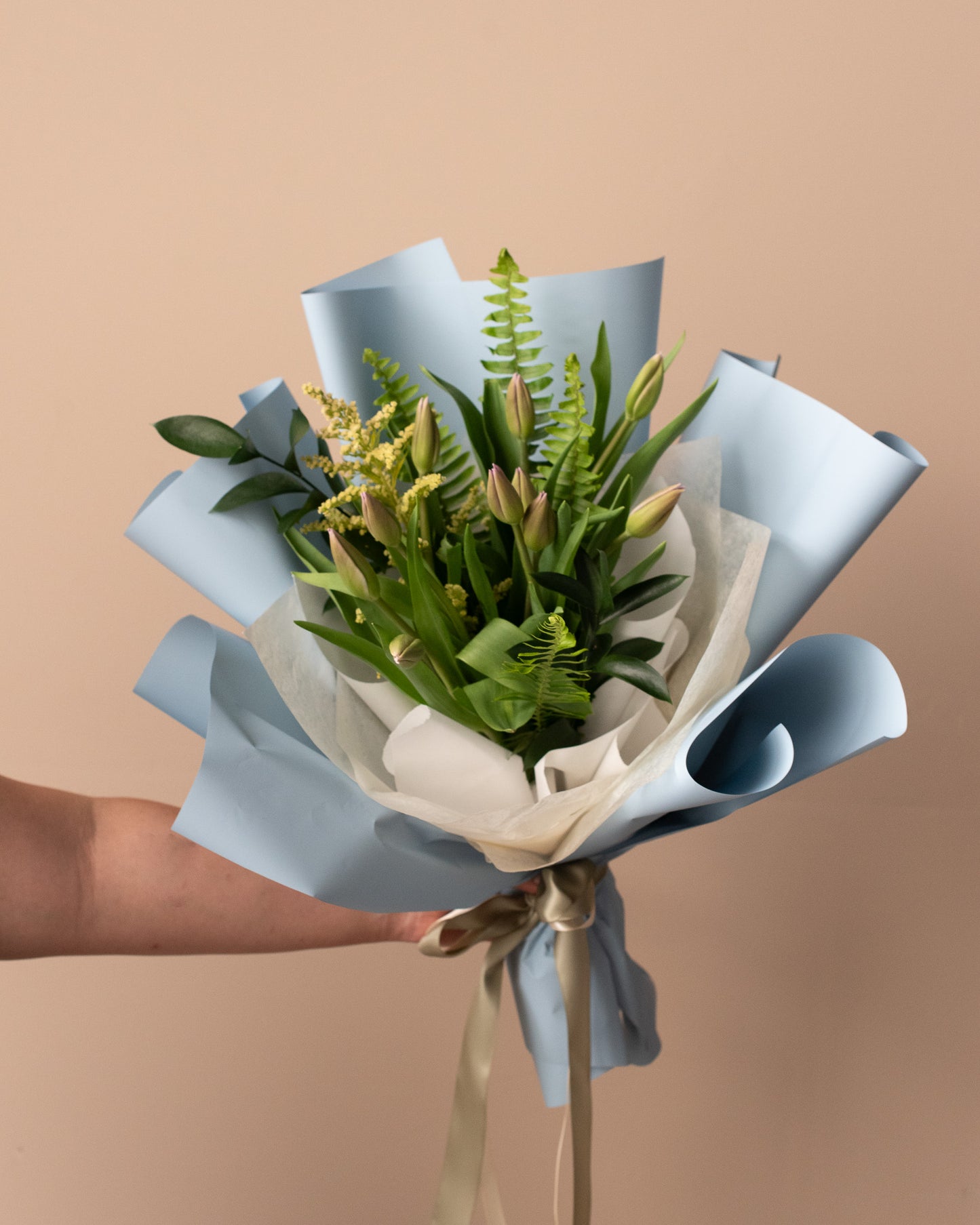 Modern floral bouquet with green leaves and buds, wrapped in blue paper by Annam Studio Toronto