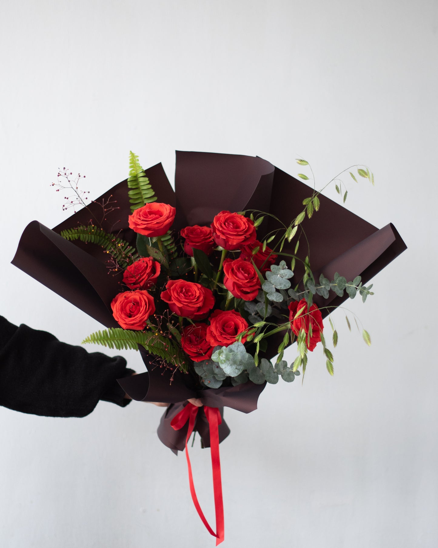 Hand holding Annam Studio modern bouquet with red roses, eucalyptus, and greenery.