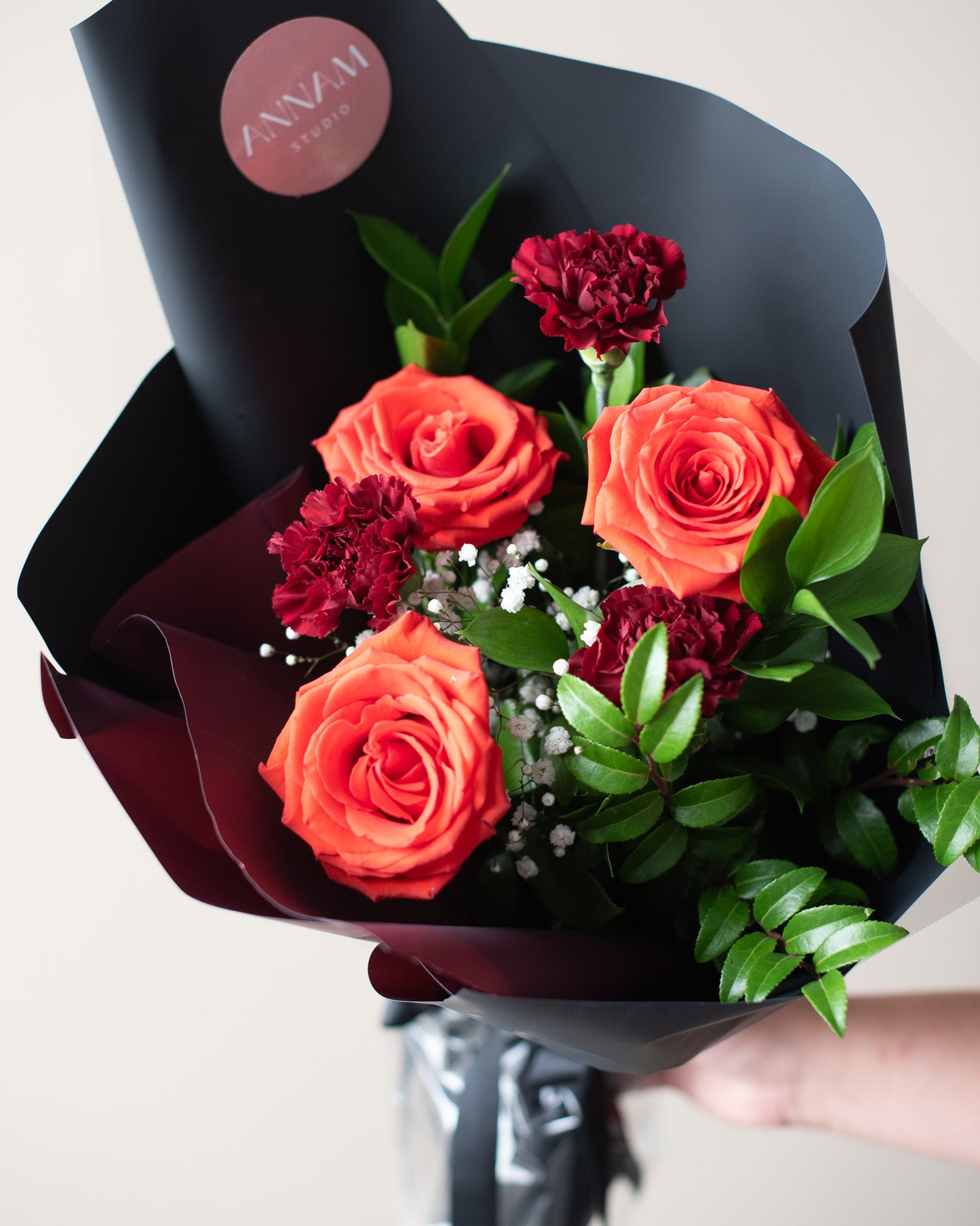 Bouquet of red roses and carnations with greenery, wrapped in black paper, for delivery or pickup in Toronto.