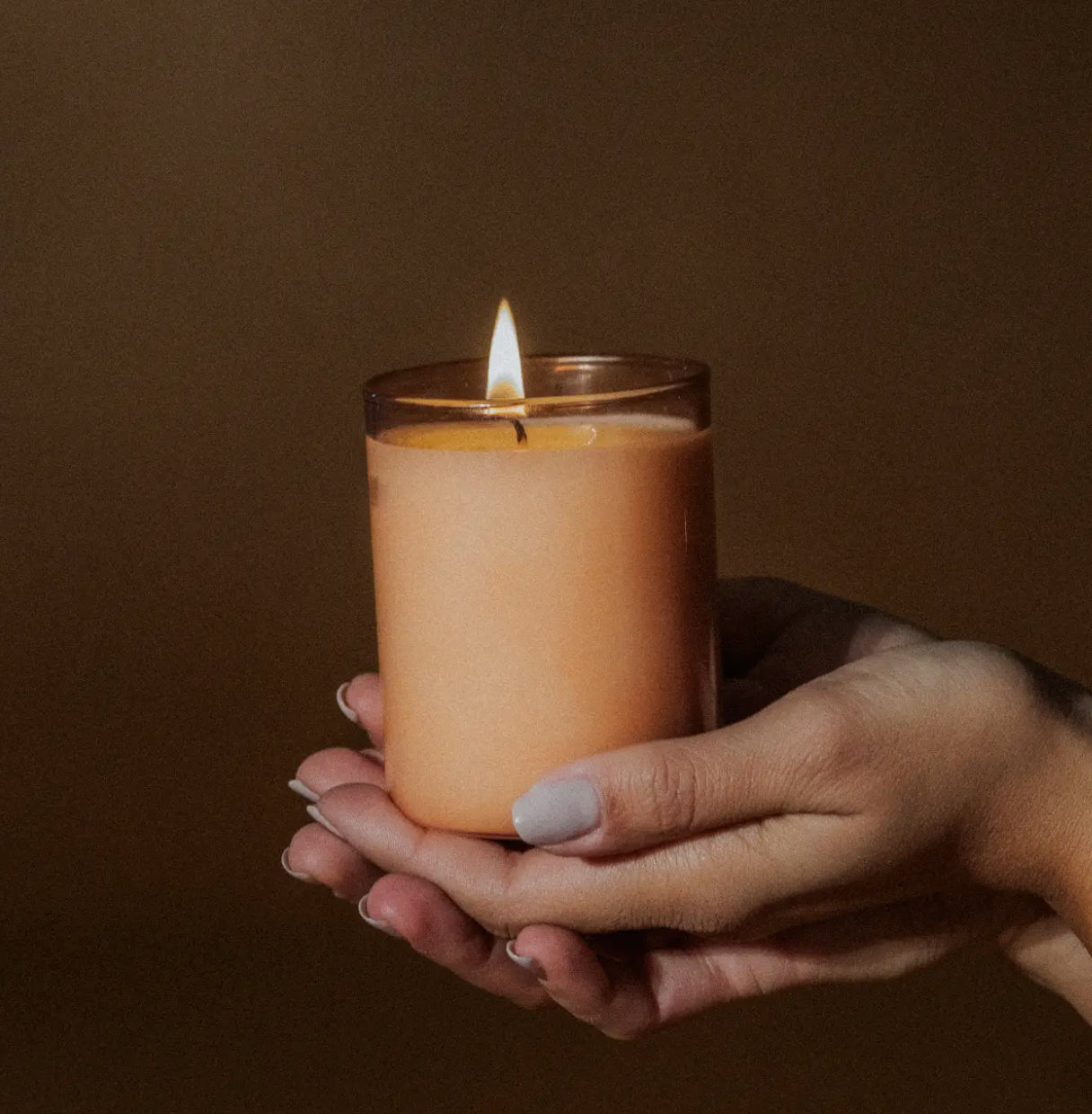 Hand holding a lit peach-colored candle, modern home decor from Annam Studio Toronto