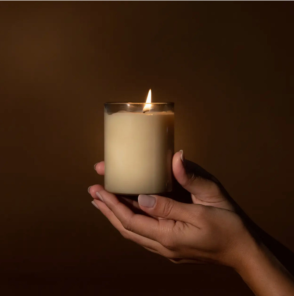 Hand holding a lit candle in a glass jar, modern gift from Annam Studio Toronto